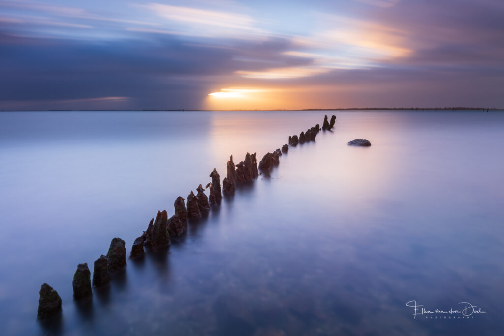 Lange sluitertijd opname van paaltjes in het water tijdens zonsondergang. 
